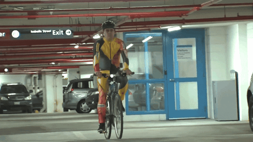 A Person Riding A Bike In A Parking Garage With A Sign That Says Exit GIF