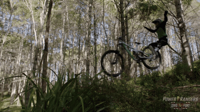 A Person Riding A Bike In The Woods With A Power Rangers Logo In The Background GIF