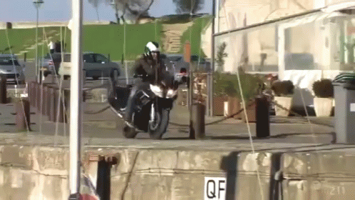A Person Riding A Motorcycle In Front Of A Building With A Sign That Says Qf GIF