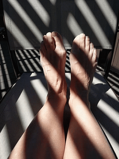 A Person 'S Feet Are Sitting On A Chair With A Shadow Of A Fence Behind Them GIF