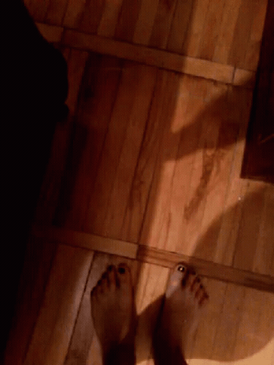 A Person 'S Feet Are Standing On A Wooden Floor In A Dark Room GIF