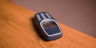 A Person 'S Hand Is Reaching For A Cell Phone On A Wooden Table . GIF