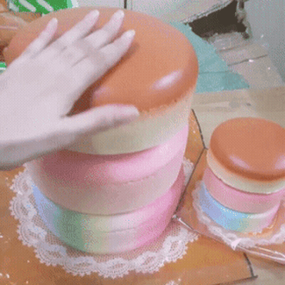 A Person 'S Hand Is Reaching Into A Stack Of Colorful Cakes On A Table GIF
