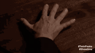 A Person 'S Hand Is Reaching Out Towards A Wooden Table . GIF