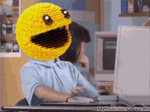 A Person Sitting At A Desk With A Yellow Smiley Face On Their Head GIF