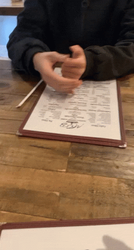 A Person Sitting At A Table With A Menu On It That Says ' Dinner ' On It GIF