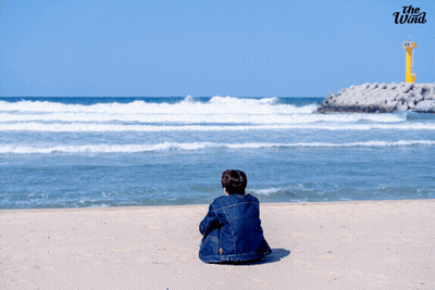 A Person Sitting On A Beach With The Wind Written On The Bottom Right GIF