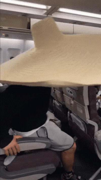 A Person Sitting On An Airplane With A Large Blanket Over Their Head GIF