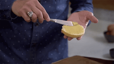 A Person Spreading Butter On A Slice Of Bread With A Knife GIF
