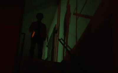 A Person Standing In A Dark Room With A Green Light Projected On The Wall GIF