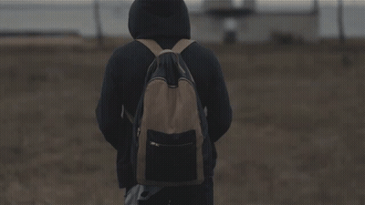 A Person Standing In A Field Holding A Knife With A Building In The Background GIF