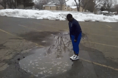 A Person Standing In A Puddle In A Parking Lot With Snow On The Ground GIF