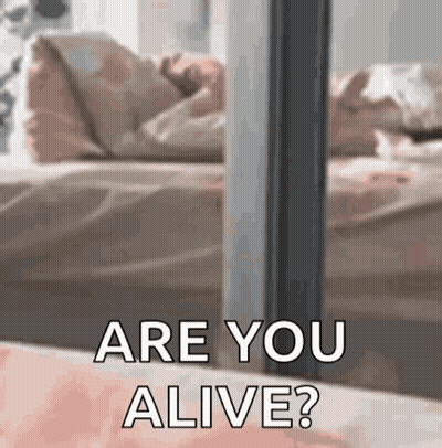 A Person Standing In Front Of A Bed With The Words `` Are You Alive '' Written On It . GIF