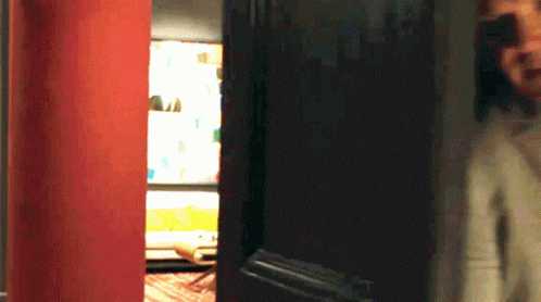 A Person Standing In Front Of A Door With A Red Wall Behind Them GIF