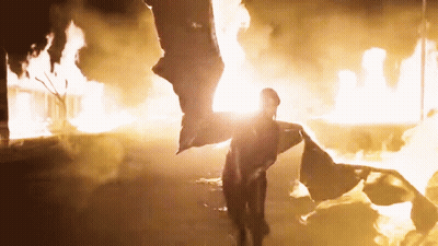 A Person Standing In Front Of A Fire With A Flag Flying In The Air GIF