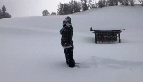 A Person Standing In The Middle Of A Snow Covered Field With A Bench In The Background GIF