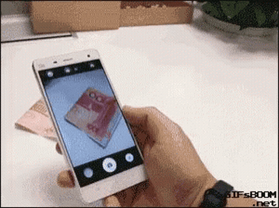A Person Taking A Picture Of A Stack Of Money With A Cell Phone GIF