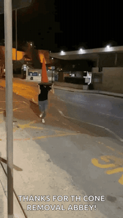 A Person Walking Down A Street With A Traffic Cone On Their Head And The Words Thanks For The Cone Removal Abbey GIF