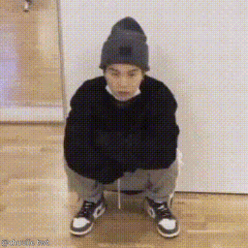 A Person Wearing A Beanie And A Sweater Is Squatting Down On The Floor . GIF