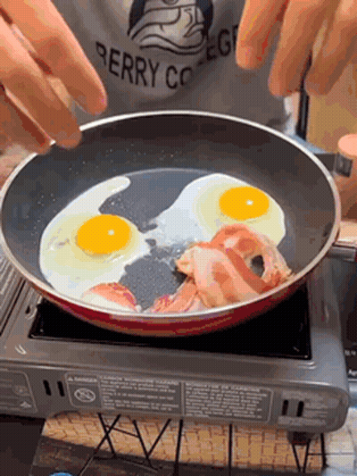 A Person Wearing A Berry College Shirt Is Cooking Eggs And Bacon GIF
