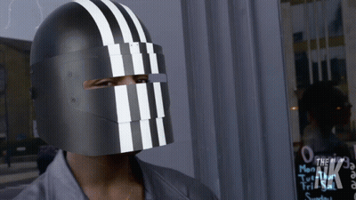 A Person Wearing A Black Helmet With White Stripes On It Stands In Front Of A Sign That Says The Nk GIF