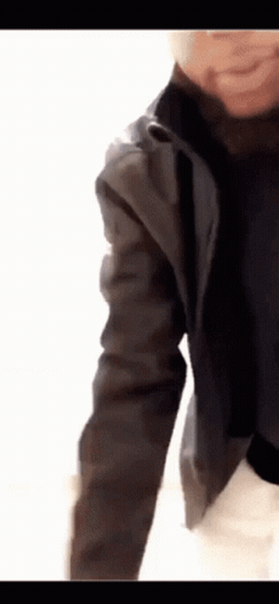 A Person Wearing A Black Jacket And A Black Turtleneck Is Standing On A White Surface . GIF