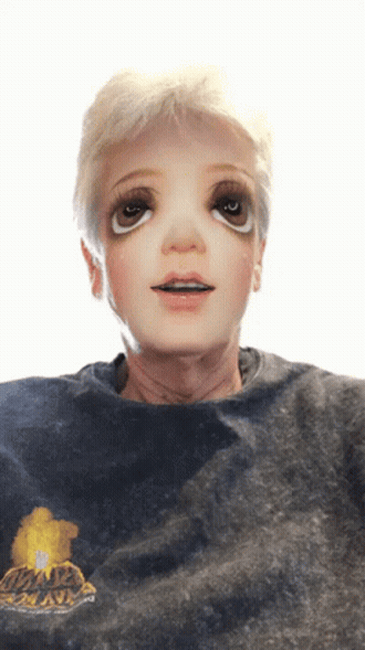 A Person Wearing A Black Shirt With A Yellow Flower On It Has A Doll Face On Their Face GIF