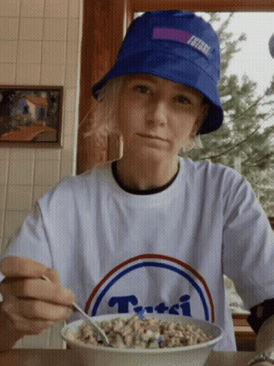 A Person Wearing A Blue Hat And A White T-Shirt With The Word Tutti On It Is Eating Cereal GIF