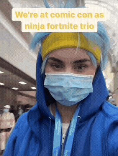 A Person Wearing A Blue Hoodie And A Mask Is Standing In A Hallway . GIF
