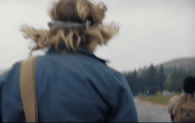 A Person Wearing A Blue Jacket Is Walking Down A Road With Trees In The Background GIF