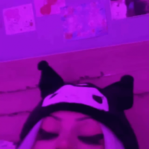 A Person Wearing A Cat Hat Is Laying On A Couch In A Pink Room . GIF