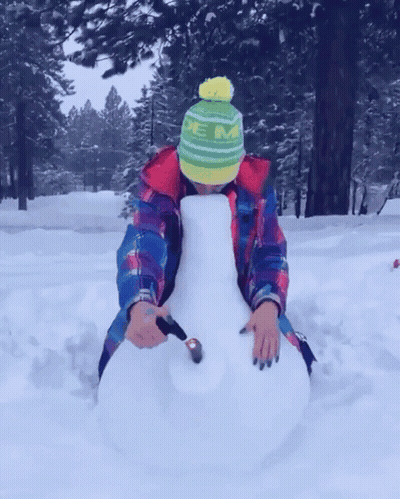 A Person Wearing A Green And Yellow Hat With The Letter M On It Is Sitting In The Snow GIF