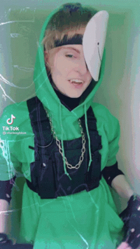 A Person Wearing A Green Hoodie And Overalls With A Mask On Their Face . GIF
