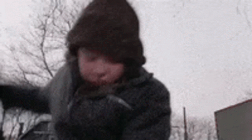 A Person Wearing A Hat And Gloves Is Walking In The Snow . GIF