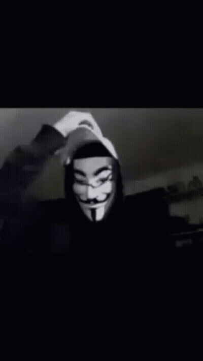 A Person Wearing A Hooded Jacket And A Anonymous Mask Is Waving At The Camera . GIF