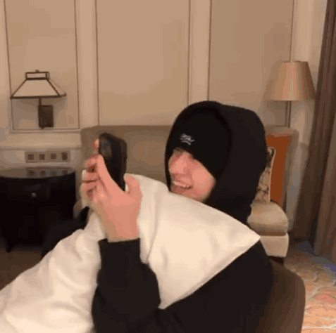 A Person Wearing A Hooded Sweatshirt And A Hat With The Letter S On It Is Holding A Cell Phone GIF