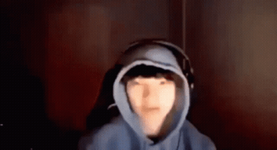 A Person Wearing A Hoodie And Headphones Is Sitting In A Dark Room . GIF