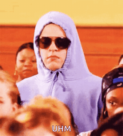 A Person Wearing A Hoodie And Sunglasses Is Standing In A Crowd Of People . GIF