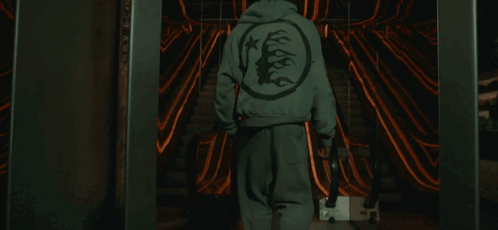 A Person Wearing A Hoodie With A Tree On The Back Walks Down An Escalator GIF