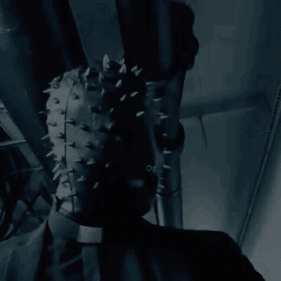 A Person Wearing A Leather Mask With Spikes On It Is Hanging From A Pipe . GIF