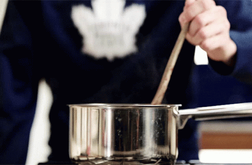A Person Wearing A Maple Leaf Sweater Stirs Something In A Pot GIF
