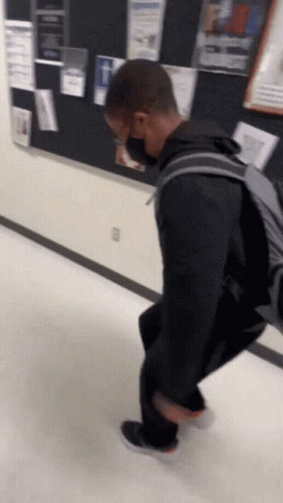 A Person Wearing A Mask And A Backpack Is Walking Down A Hallway GIF