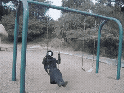 A Person Wearing A Mask Sits On A Swing In A Park GIF