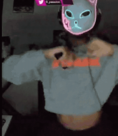 A Person Wearing A Neon Cat Mask And A Crop Top Is Taking Off Their Shirt . GIF