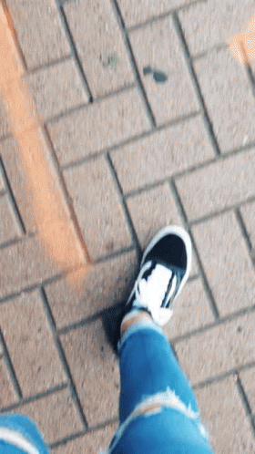 A Person Wearing A Pair Of Black And White Sneakers Is Standing On A Brick Sidewalk GIF