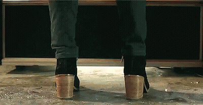 A Person Wearing A Pair Of Heeled Boots Is Standing On A Concrete Floor . GIF