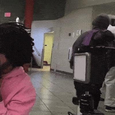 A Person Wearing A Pink Hoodie Is Standing In A Hallway With A Camera GIF