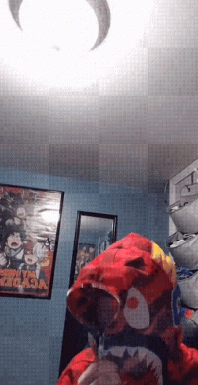 A Person Wearing A Red Shark Hoodie In A Room With A Poster That Says My Hero Academia GIF