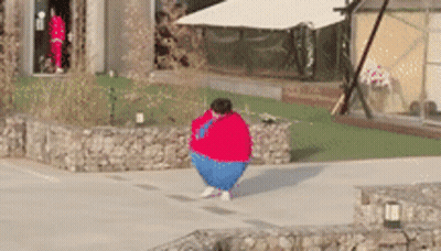 A Person Wearing A Red Sweater And Blue Pants Is Standing On A Sidewalk . GIF
