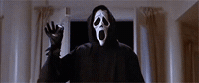 A Person Wearing A Scream Mask And A Hooded Jacket Is Standing In A Dark Room . GIF